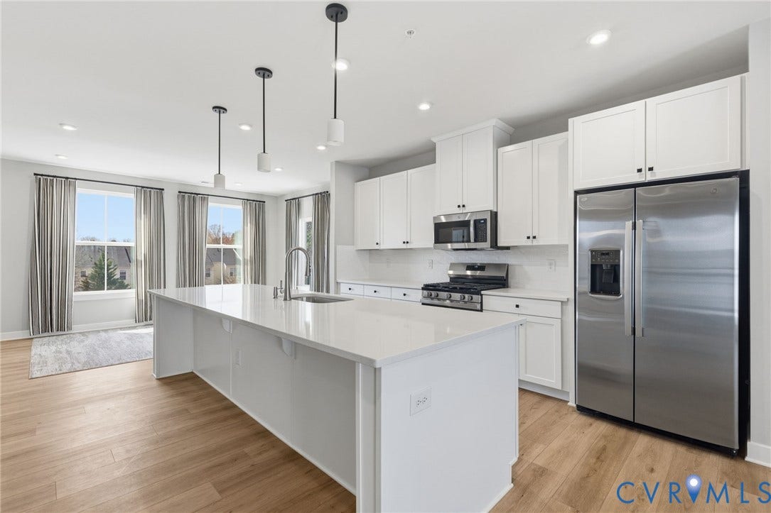 Gourmet kitchen featuring a large central island with integrated sink, stainless steel appliances, white cabinetry, and wood-finish flooring