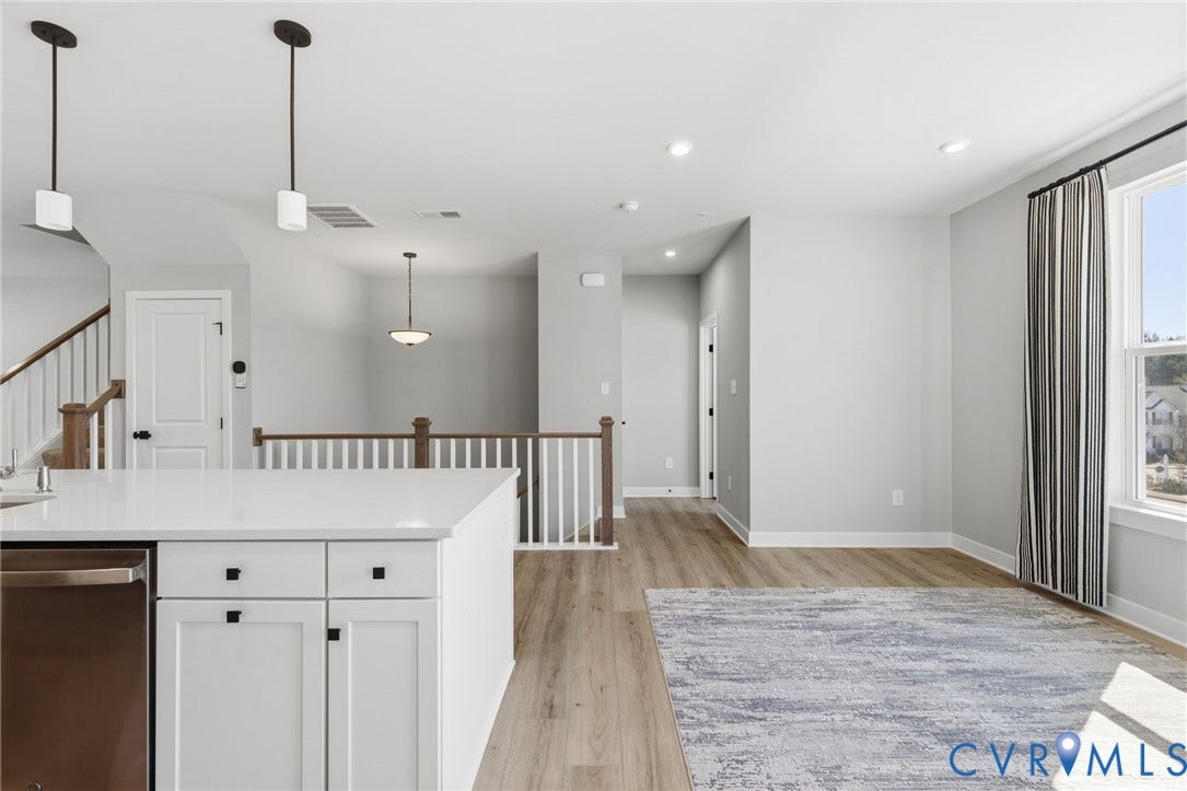 Open-concept main level featuring wood-finish flooring, white cabinetry with dark hardware, a white countertop, and recessed lighting