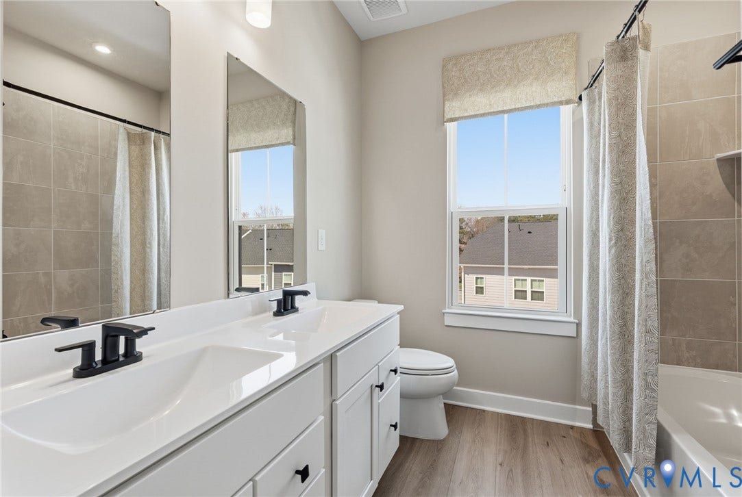 Double vanity with undermount sinks and matte black faucets, white cabinetry, wood-finish flooring, and a tiled tub surround