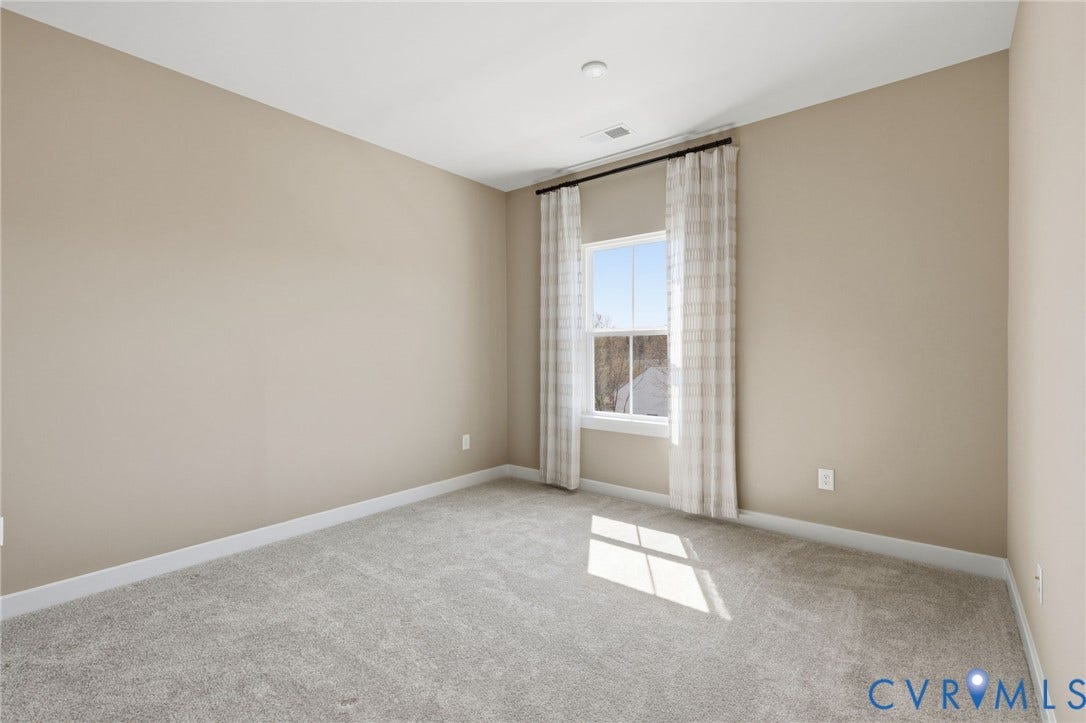 Bright and spacious bedroom flooded with natural light through expansive windows framed by neutral curtains