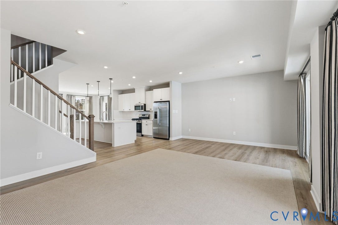 Open-concept living area featuring wood-finish flooring, recessed lighting, and a modern kitchen with stainless steel appliances and white cabinetry