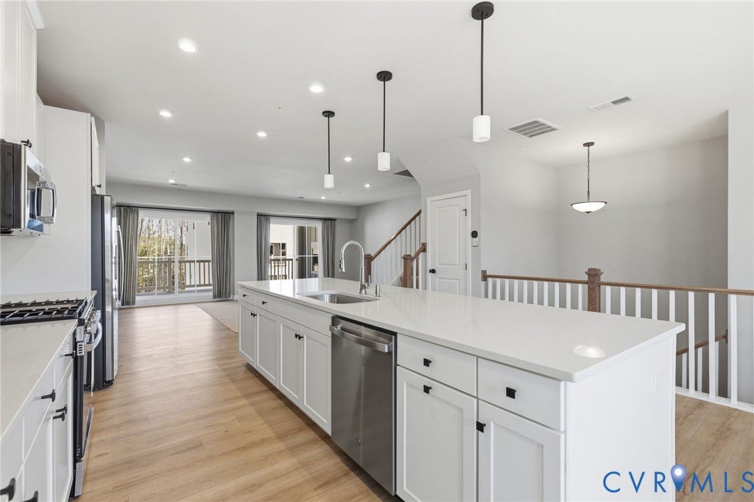 Spacious kitchen featuring an expansive center island with an undermount sink, stainless steel appliances, and wood-finish flooring