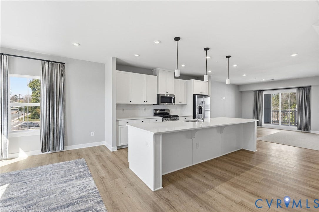 Open-concept kitchen with a large island, white cabinetry, integrated stainless steel appliances, and wood-finish flooring throughout