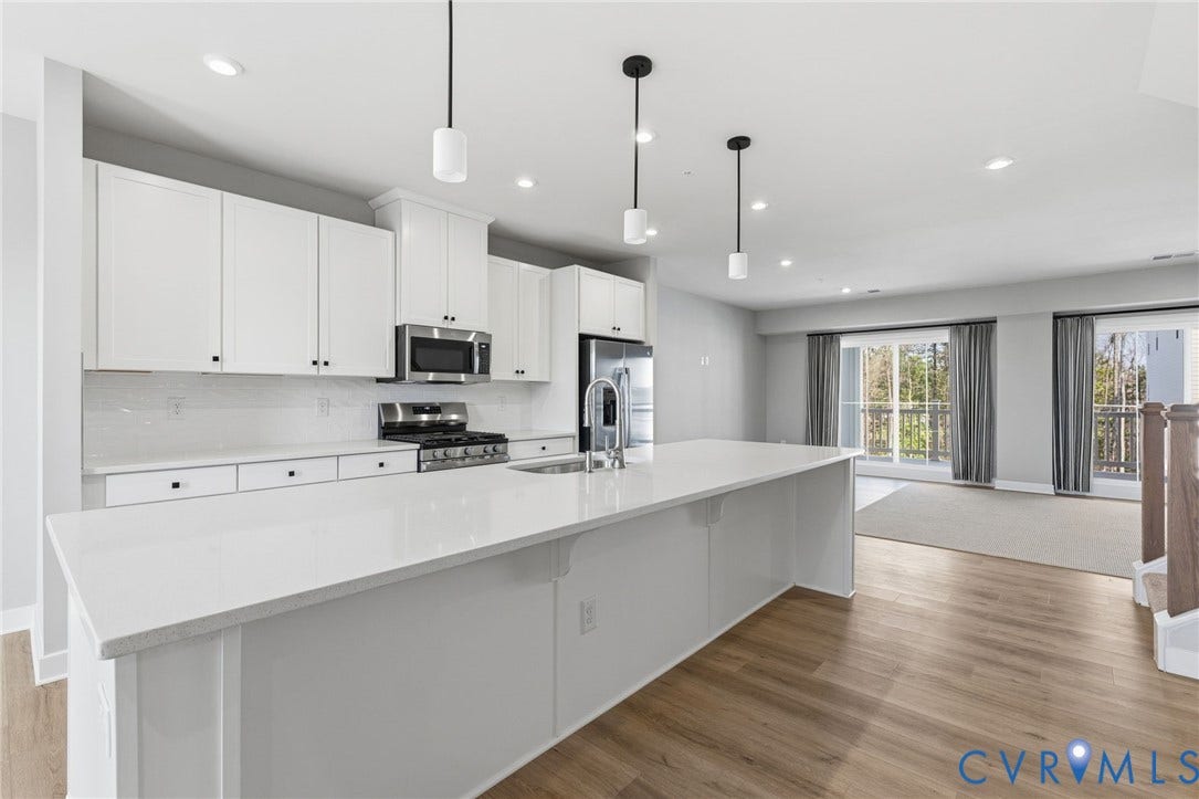 Modern kitchen featuring white cabinetry, stainless steel appliances, a large center island with a sink, and wood-finish flooring