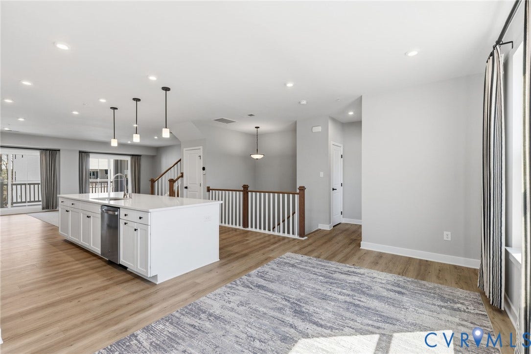 Spacious open-concept living area featuring wood-finish flooring, recessed lighting, and a kitchen island with white cabinetry and a stainless steel appliance