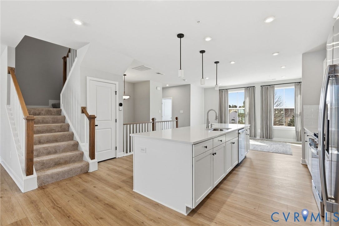 Kitchen featuring a central island with a sink and pendant lighting, stainless steel appliances, light wood-finish flooring, and white cabinetry
