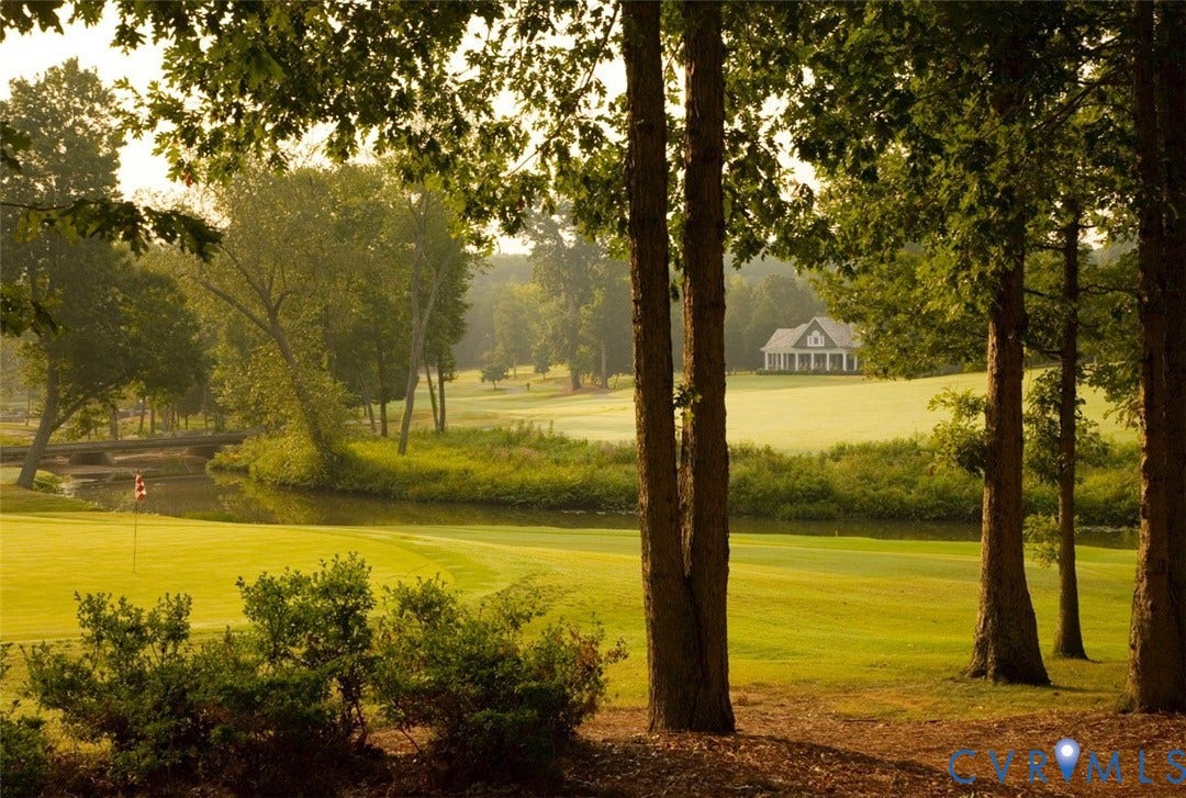 Expansive golf course setting featuring manicured greens, mature trees, and a tranquil water feature