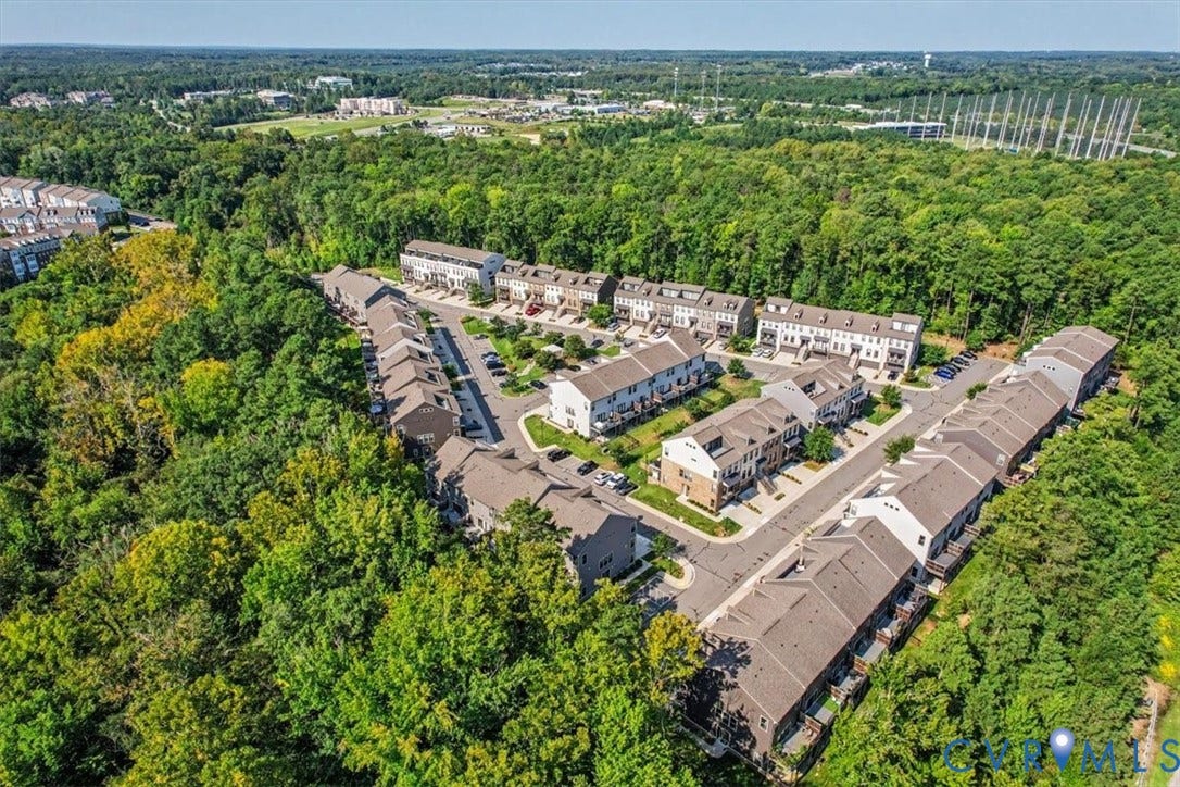 1141 Broad Hill Trace, Saunders Station Townes, Henrico, VA 23233 Aerial perspective showcasing a residential community within a wooded setting, featuring multiple townhome structures and established roadways