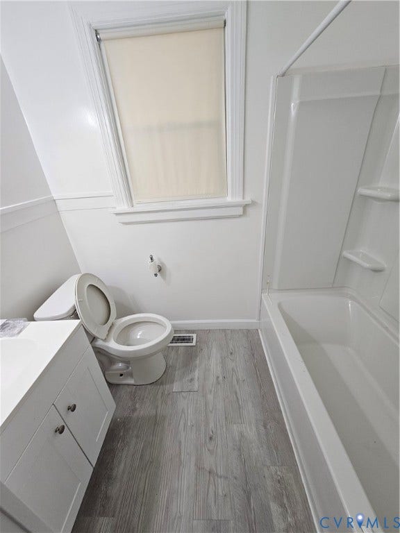 Bathroom featuring a single window, white vanity with cabinet storage, a toilet, a bathtub with shower surround, and wood-finish flooring