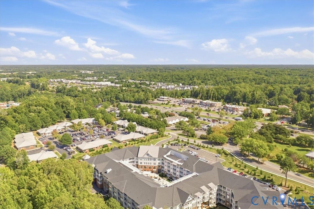 Expansive multi-story residential building with a large central courtyard, surrounded by mature trees, and multiple parking areas