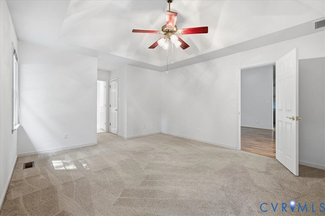 Tray ceiling, ceiling fan with light fixture, neutral carpeting, window with natural light, and a paneled interior door