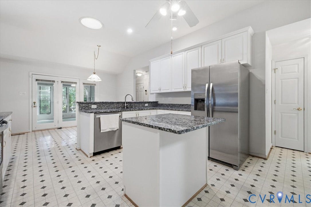 White cabinetry, granite countertops, stainless steel appliances, central island, and patterned tile flooring