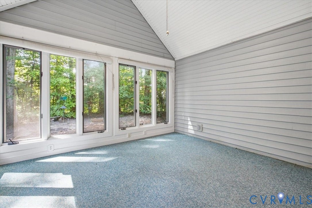 Vaulted ceiling, paneled walls, full-height windows, and light blue carpeting