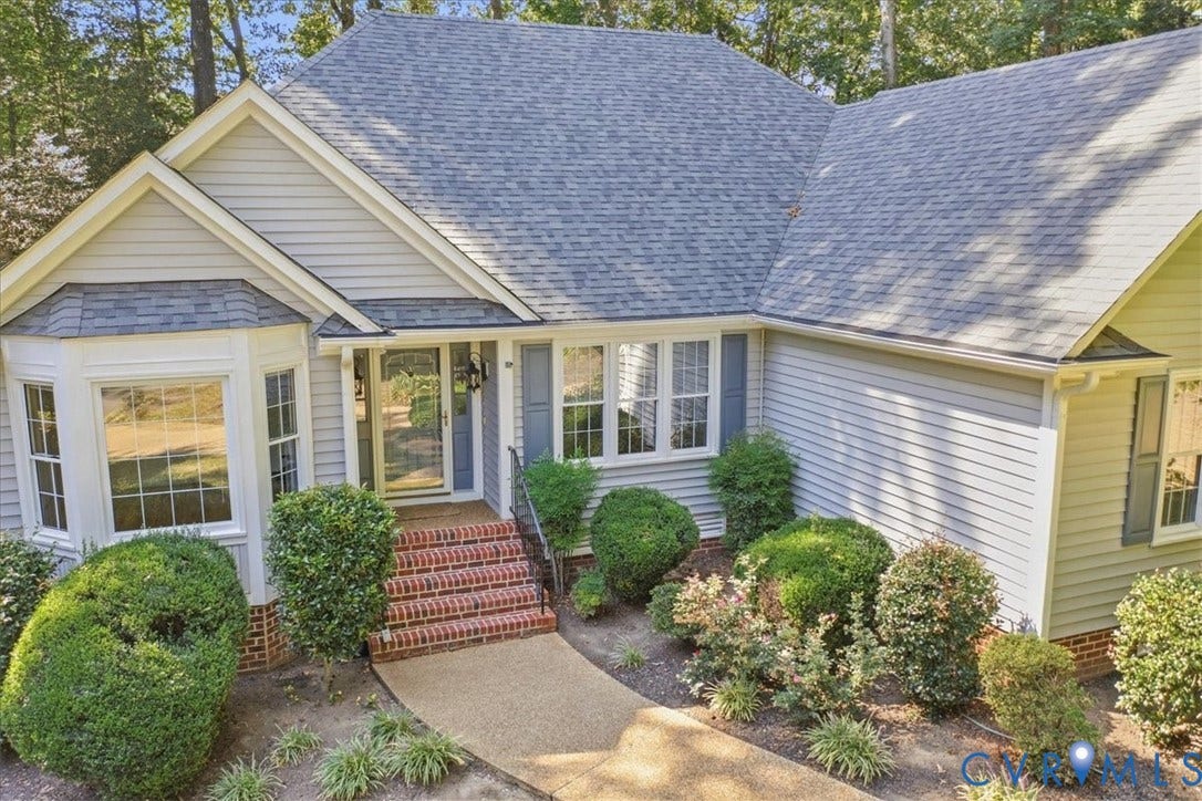 Light gray siding exterior with a multi-gabled roof, prominent bay window, and a brick-clad entry staircase
