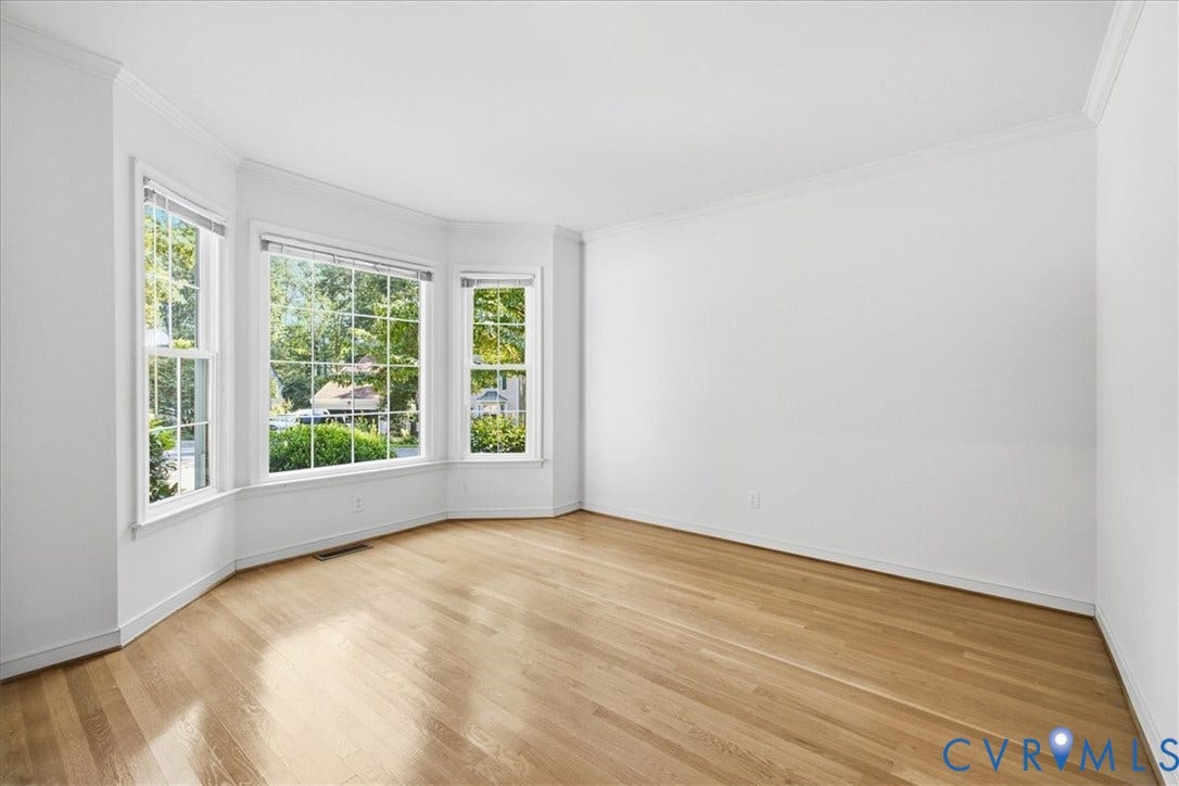 Hardwood flooring, bay window with multiple panes, crown molding, and white wall finishes
