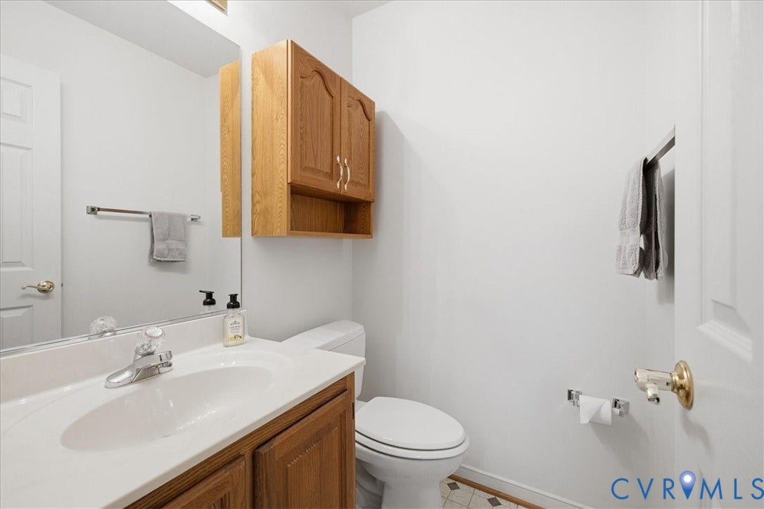 White vanity with a single basin sink, chrome faucet, and wood-finish cabinetry
