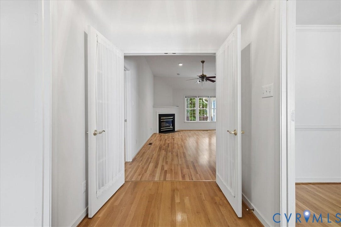 Double French doors opening to an interior space with wood-finish flooring, a vaulted ceiling, a ceiling fan, a fireplace, and a window