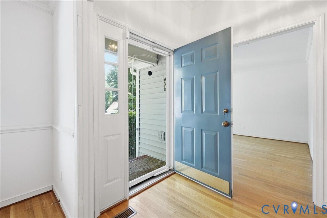Paneled front door, sidelight with multiple panes, wood-finish flooring, white wall paneling, white door trim