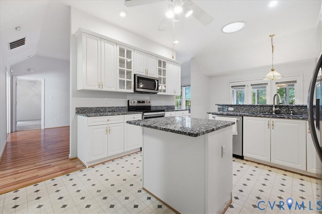 Kitchen featuring white cabinetry, dark speckled countertops, a central island, stainless steel appliances, and a vaulted ceiling with a skylight