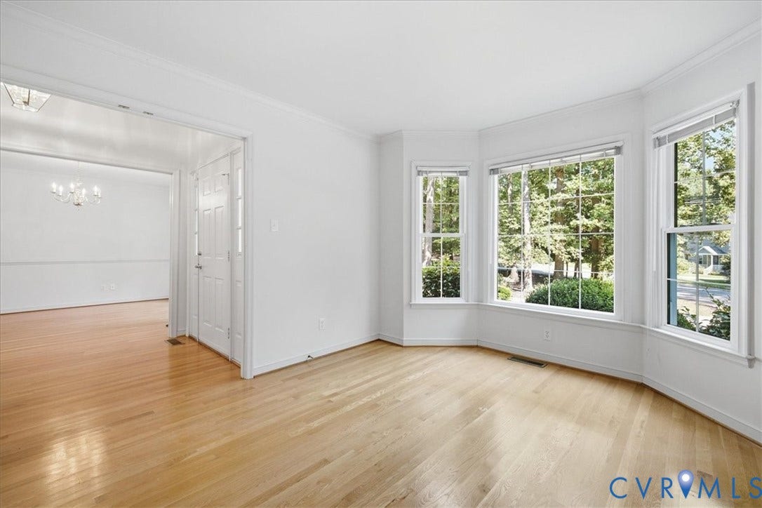 Hardwood flooring throughout, bay window with multiple panes, crown molding, and a chandelier in the adjacent room