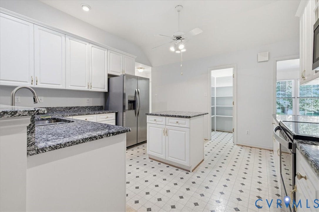 White cabinetry with gold-tone hardware, dark patterned countertops, stainless steel appliances, a center island, and patterned flooring