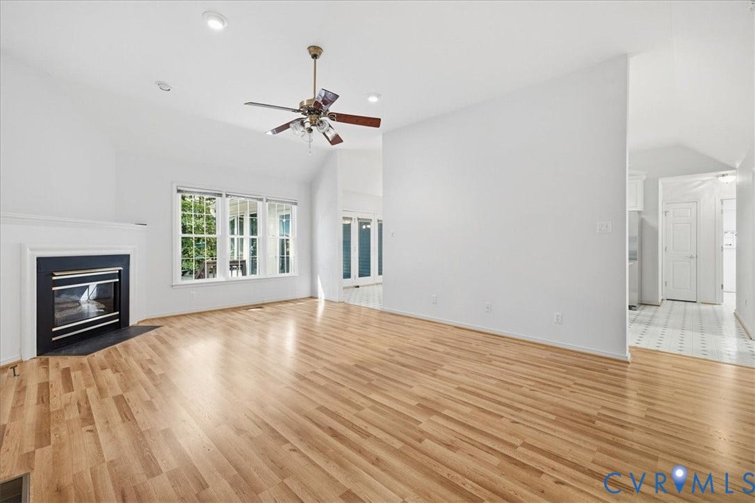 Spacious living area featuring wood-finish flooring, a fireplace with a black surround, vaulted ceilings, and recessed lighting