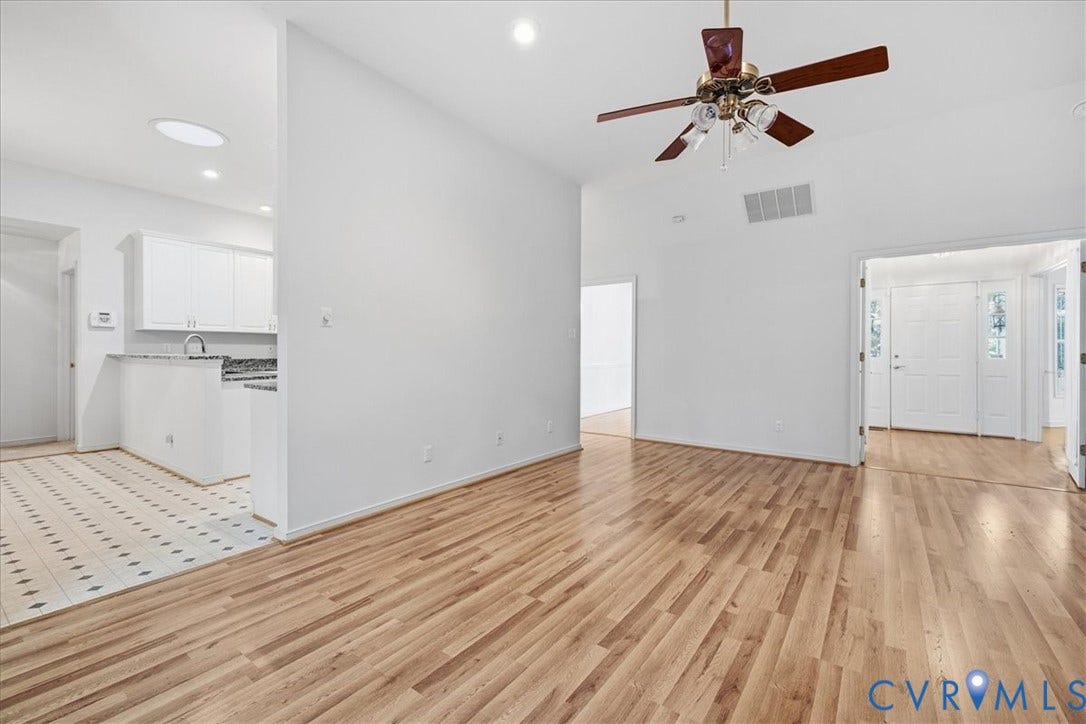 Vaulted ceiling with a ceiling fan, light wood-finish flooring, white walls, kitchen with white cabinetry, and white entry doors with decorative glass panels