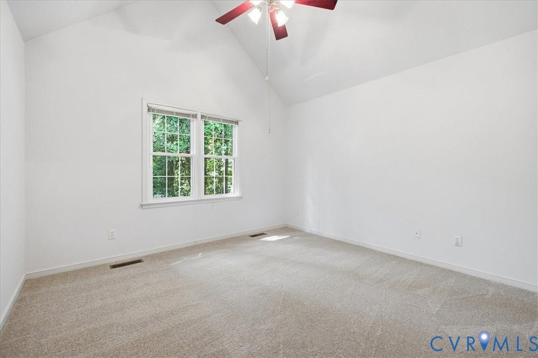 Vaulted ceiling, ceiling fan with light, dual-pane window, wall-to-wall carpeting, and neutral paint