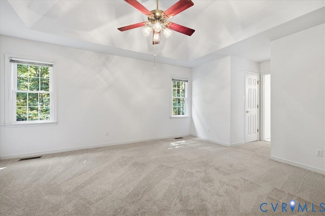 Tray ceiling with a ceiling fan, two double-hung windows, soft gray carpet, and a white paneled door