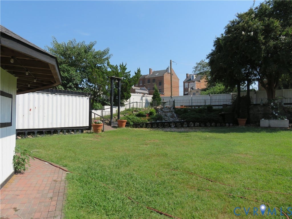 136 River Street, Petersburg, VA 23803 Expansive grassy area with a brick paver pathway, elevated landscaping featuring mature shrubs, and a partial view of a white structure with an overhang