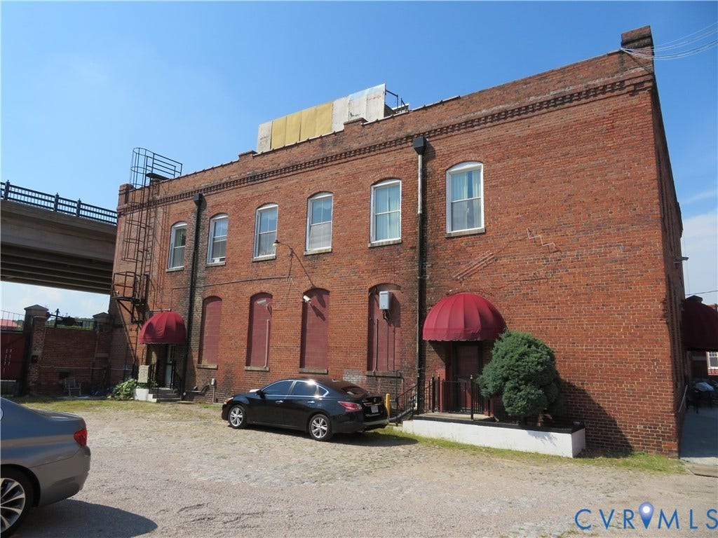 136 River Street, Petersburg, VA 23803 Brick exterior, arched window openings, red fabric awnings, metal fire escape, paved parking area
