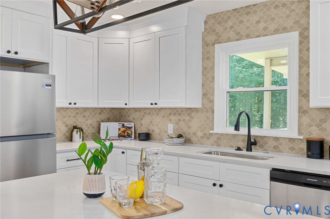 White shaker-style cabinetry, scalloped backsplash tiling, stainless steel appliances, white countertops, and a black gooseneck faucet