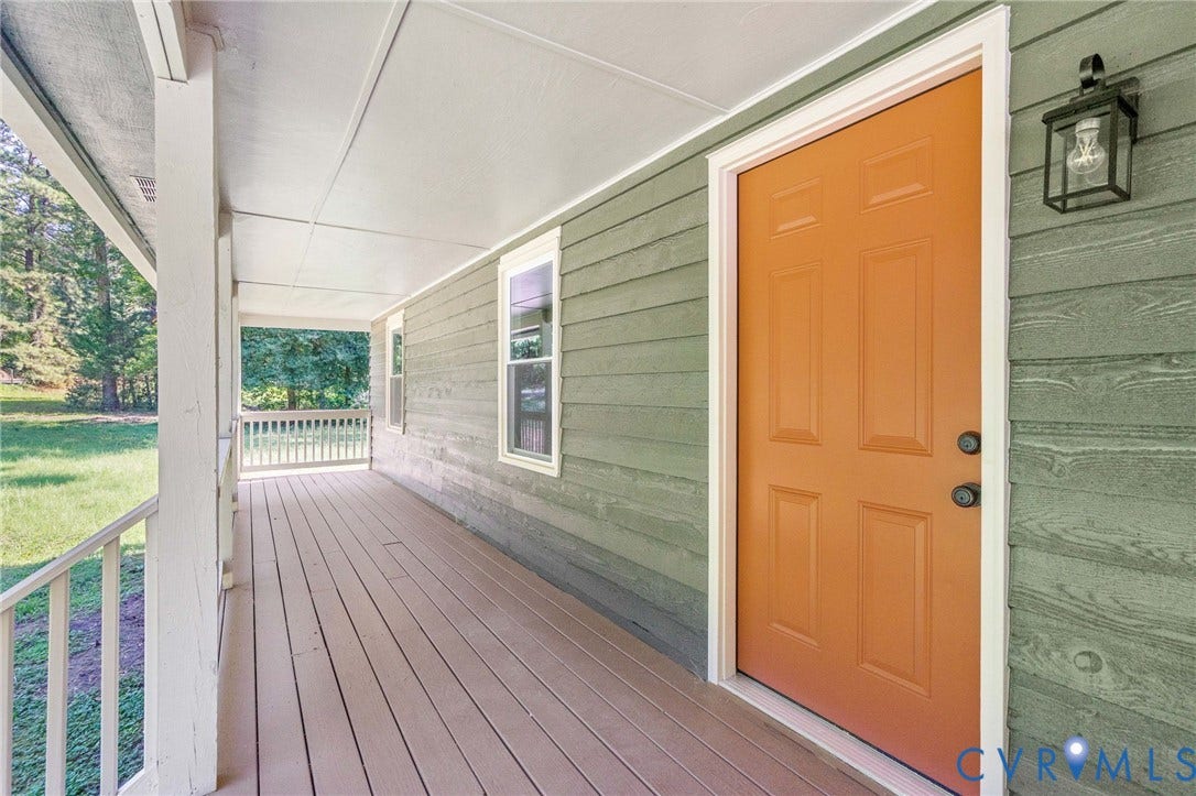 Expansive covered porch with wood-finish flooring, a vibrant orange paneled entry door, and a classic exterior light fixture