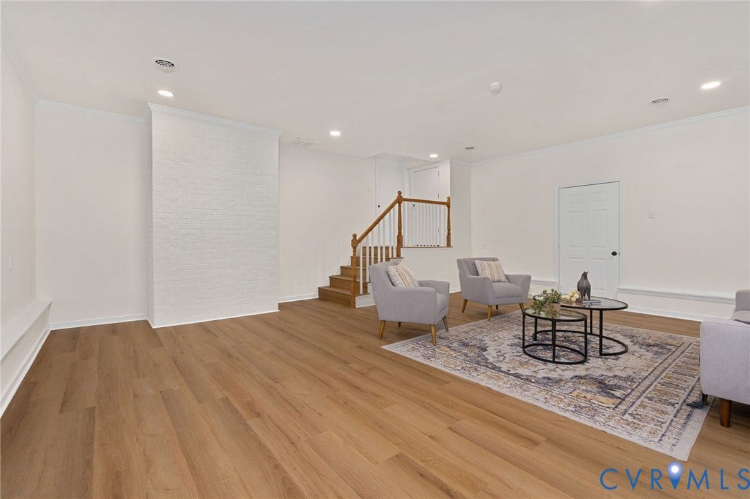 Expansive room featuring wood-finish flooring, white painted brick accent wall, recessed lighting, and a staircase with wood treads and a white banister