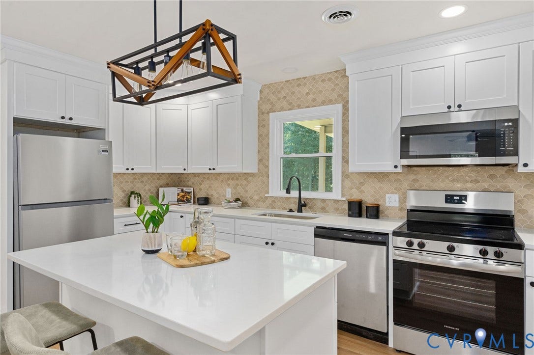 White shaker cabinetry, stainless steel appliances, central island with solid surface countertop, textured tile backsplash, and a modern rectangular chandelier