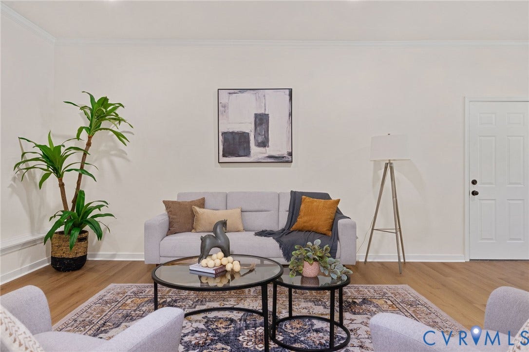 Warm wood-finish flooring, crisp white walls, crown molding, and a solid paneled interior door with black hardware
