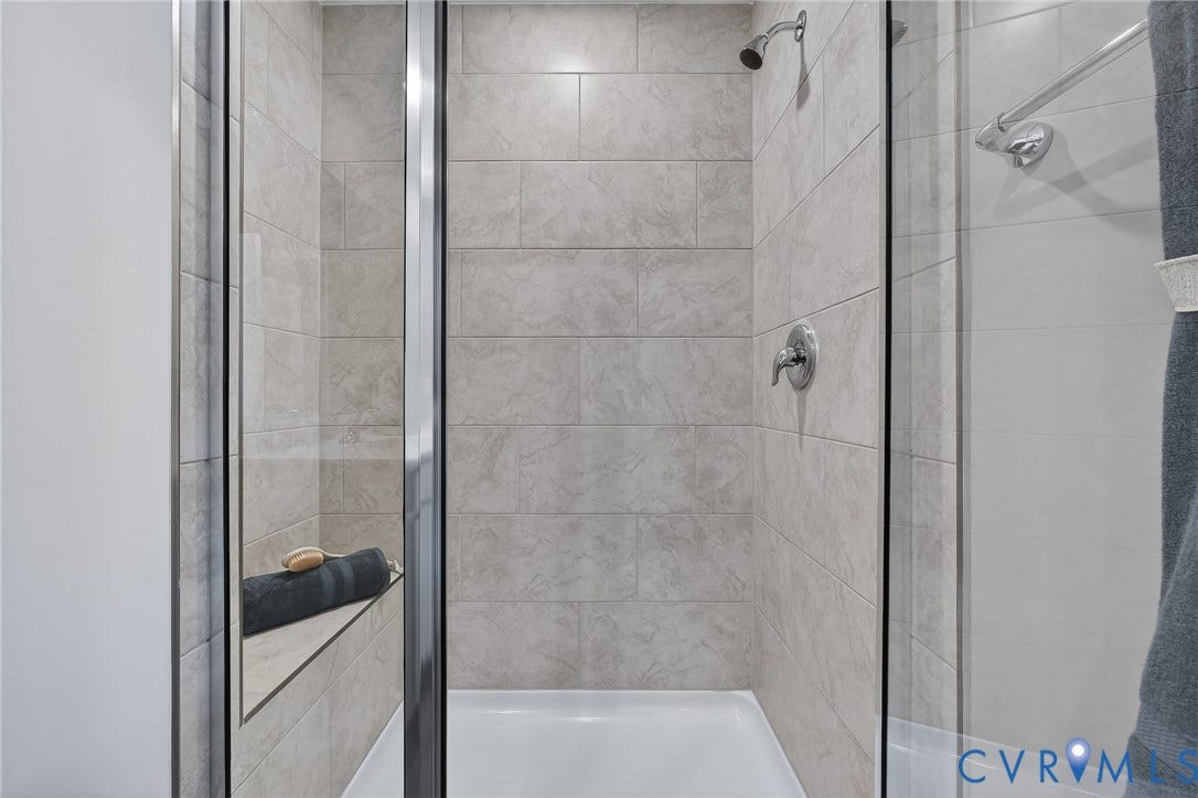 6138 Hull Street Road, Richmond, VA 23224 Glass-enclosed shower with a built-in bench, neutral tile surround, and chrome fixtures