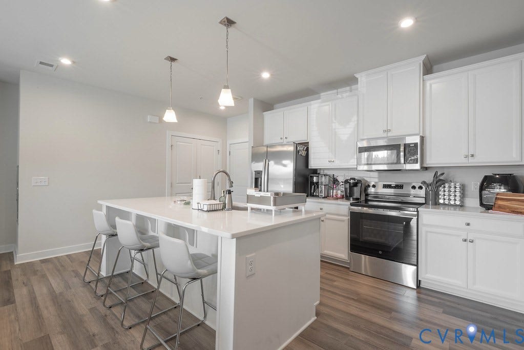 4000 Maze Runner Drive, #101, Midlothian, VA 23112 Kitchen featuring a large island with seating, white cabinetry, integrated stainless steel appliances, pendant lighting, and wood-finish flooring