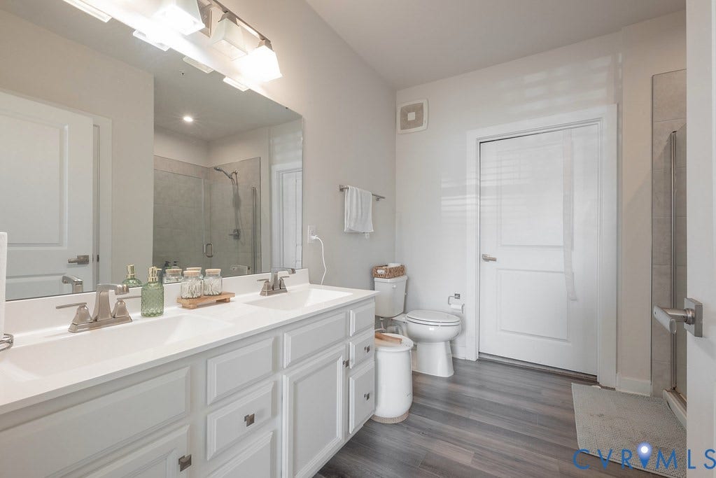 4000 Maze Runner Drive, #101, Midlothian, VA 23112 Double vanity with white cabinetry, wood-finish flooring, and a glass-enclosed shower
