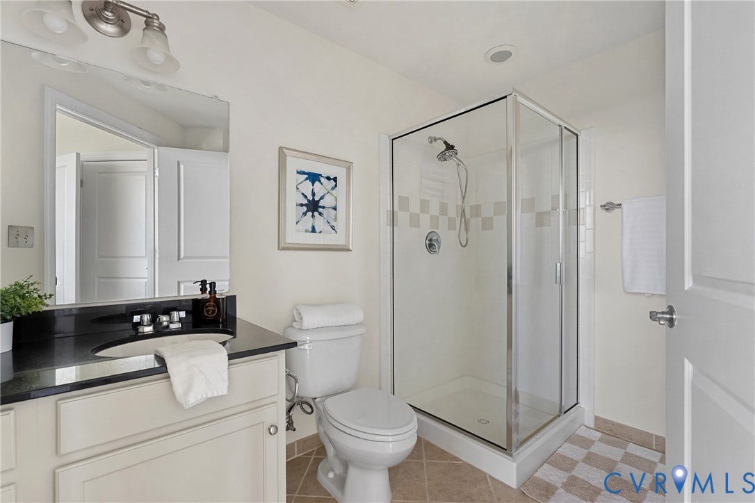 1101 Haxall Point, #U514, Richmond, VA 23219 Vanity with a black countertop and oval undermount sink, glass-enclosed shower with tiled accents, and ceramic tile flooring