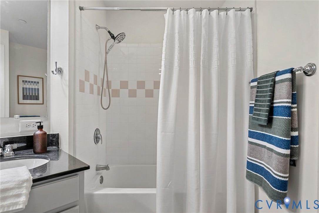 1101 Haxall Point, #U514, Richmond, VA 23219 Bathtub with tiled surround and decorative accent band, dark stone-finish vanity countertop with integrated sink, and chrome fixtures