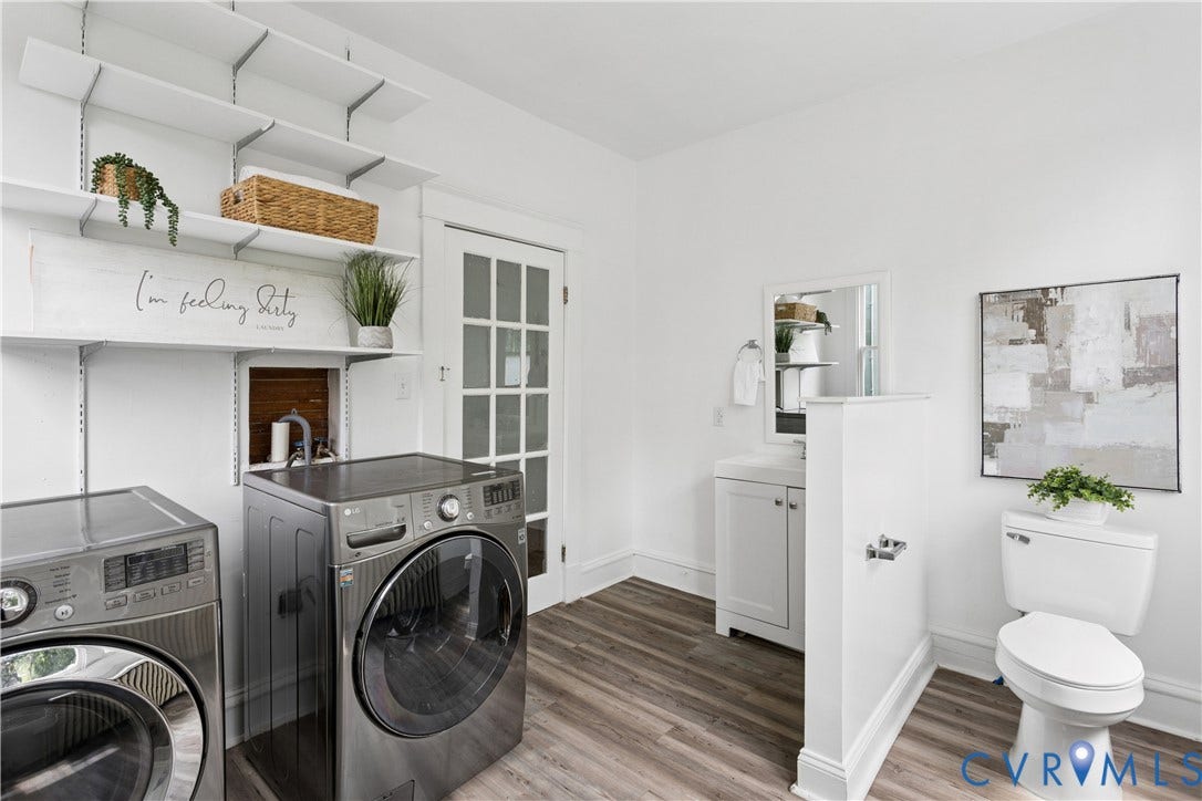 1304 Bainbridge Street, Manchester, Richmond, VA 23224 White walls with wood-finish flooring, a white vanity with mirror, white toilet, and adjustable wall-mounted shelving
