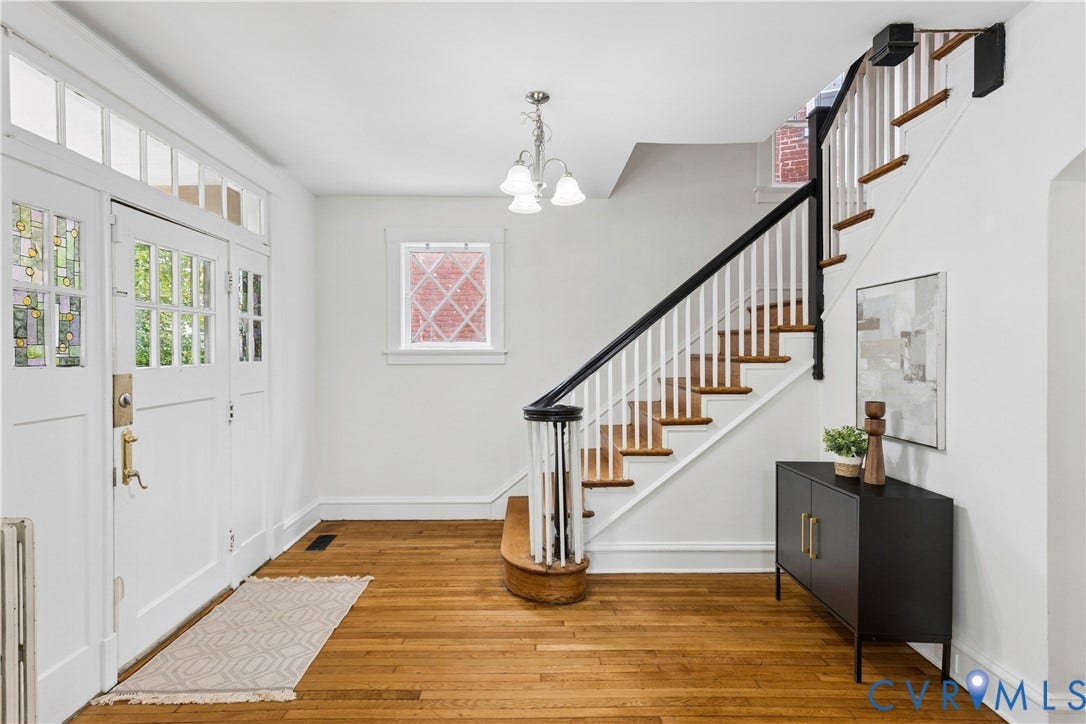 1304 Bainbridge Street, Manchester, Richmond, VA 23224 Hardwood flooring, white painted walls, wood-finish staircase with white risers and dark handrail, decorative glass paneled front door, overhead chandelier
