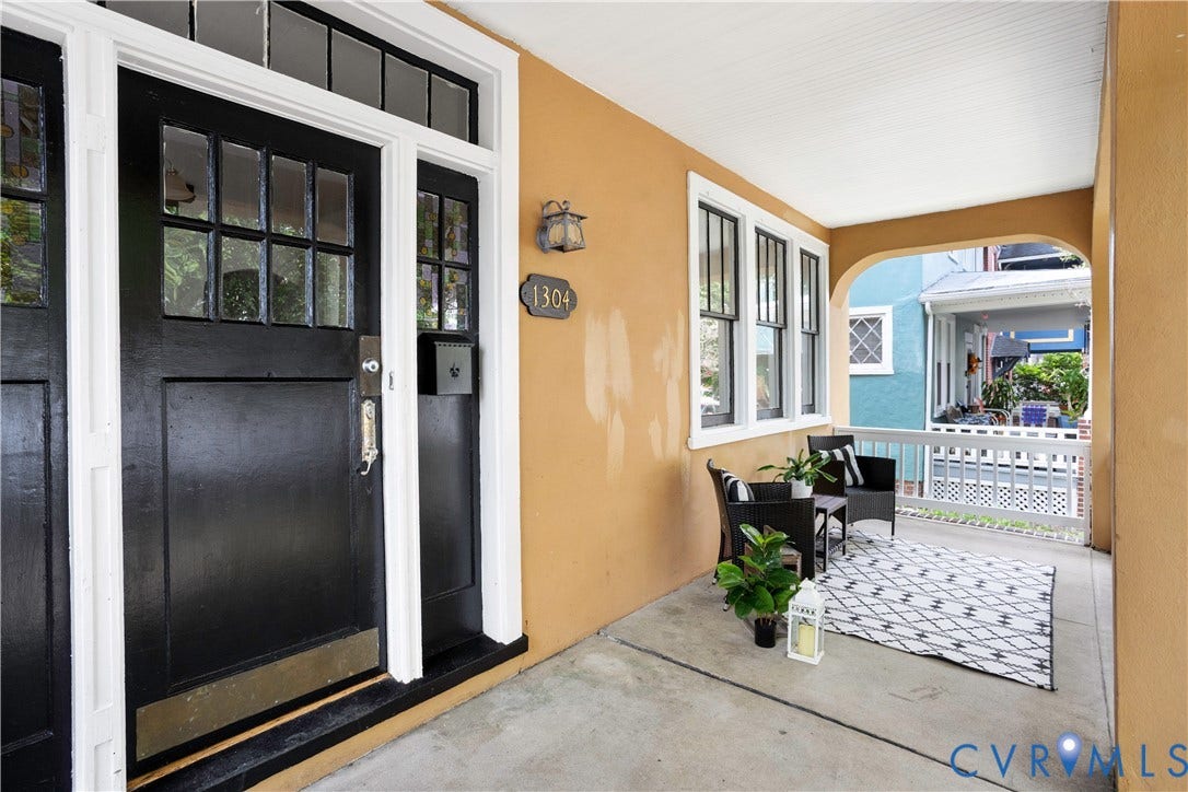 1304 Bainbridge Street, Manchester, Richmond, VA 23224 Covered front porch featuring a black paneled entry door with transom window, white trim, and a wall-mounted light fixture
