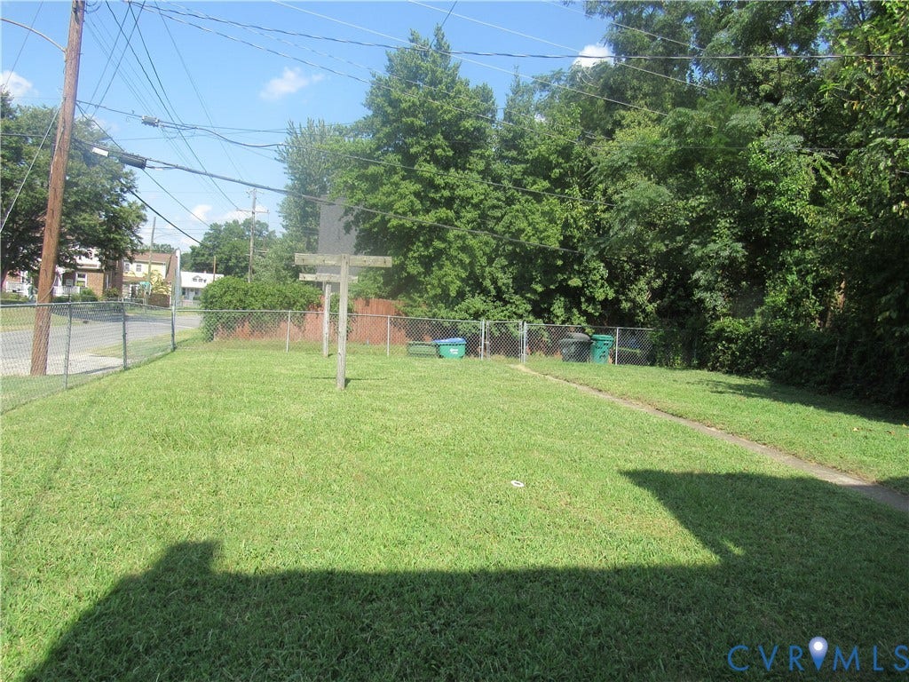 Expansive grassy yard with chain-link fencing, mature trees, and a privacy fence