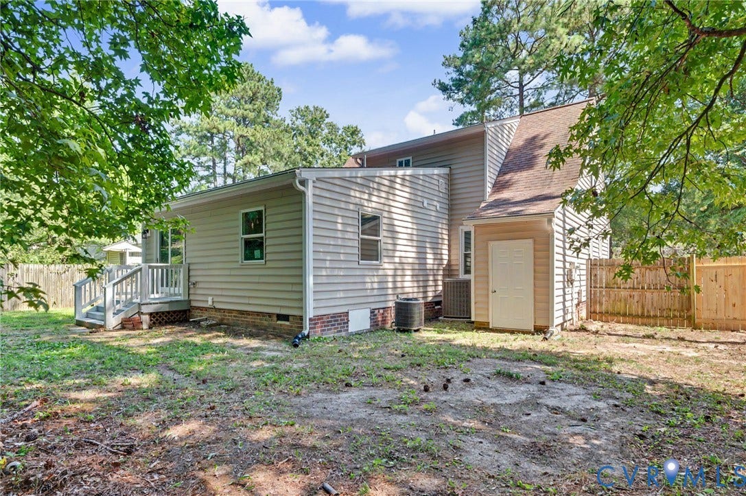 Exterior featuring neutral siding, partial brick foundation, elevated deck, attached storage unit, and wood fencing