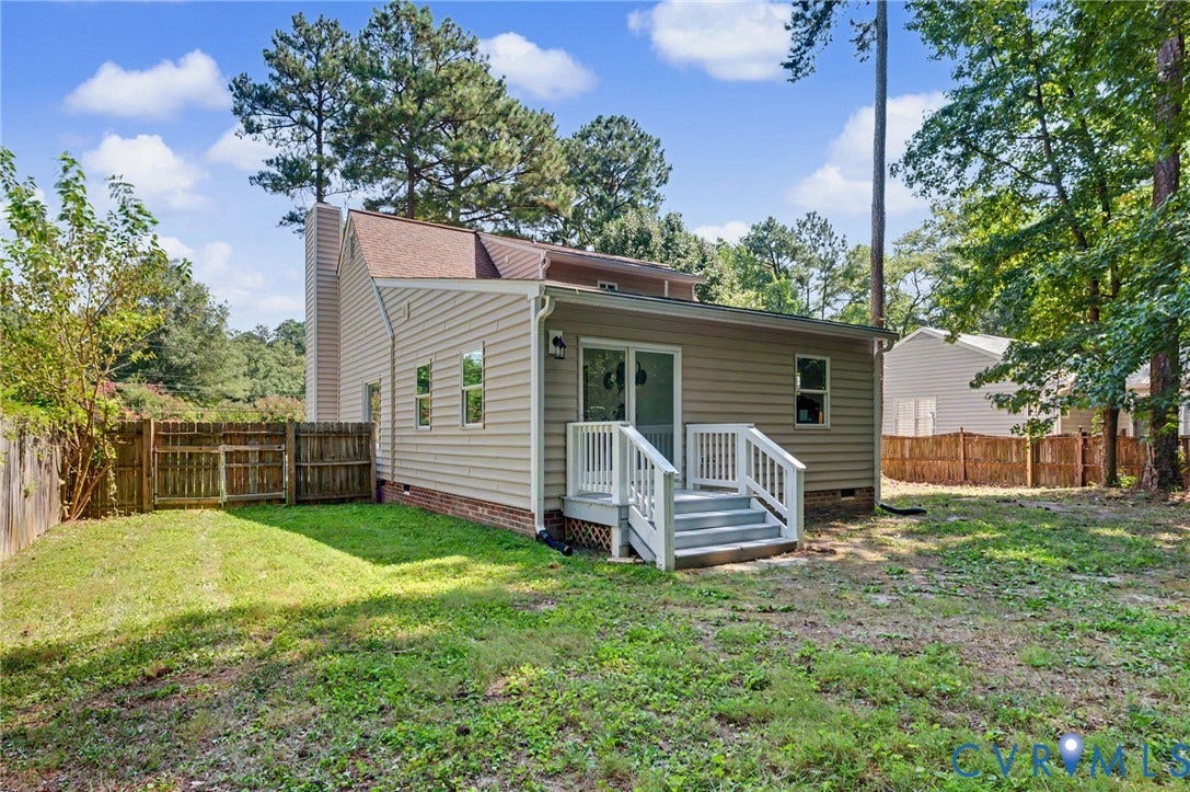Rear exterior featuring siding, an attached deck with railings, a sliding glass door, and a privacy fence