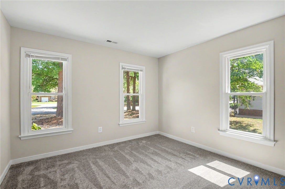 Neutral-toned walls, three double-hung windows, and gray patterned carpeting