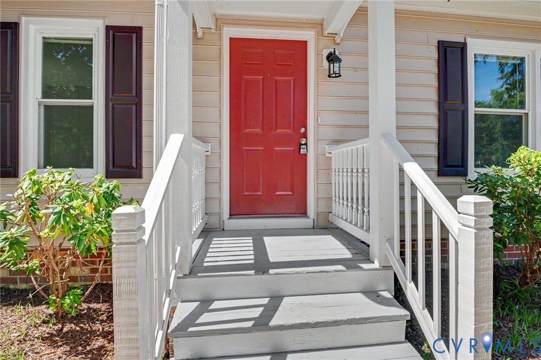 Red entry door, white porch railing, exterior wall siding, and dark window shutters
