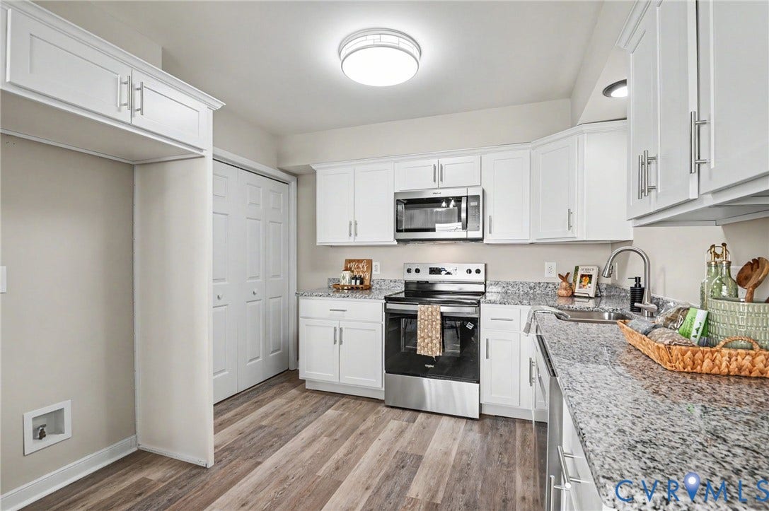 Contemporary kitchen featuring white cabinetry, granite countertops, stainless steel appliances, wood-finish flooring, and a built-in pantry